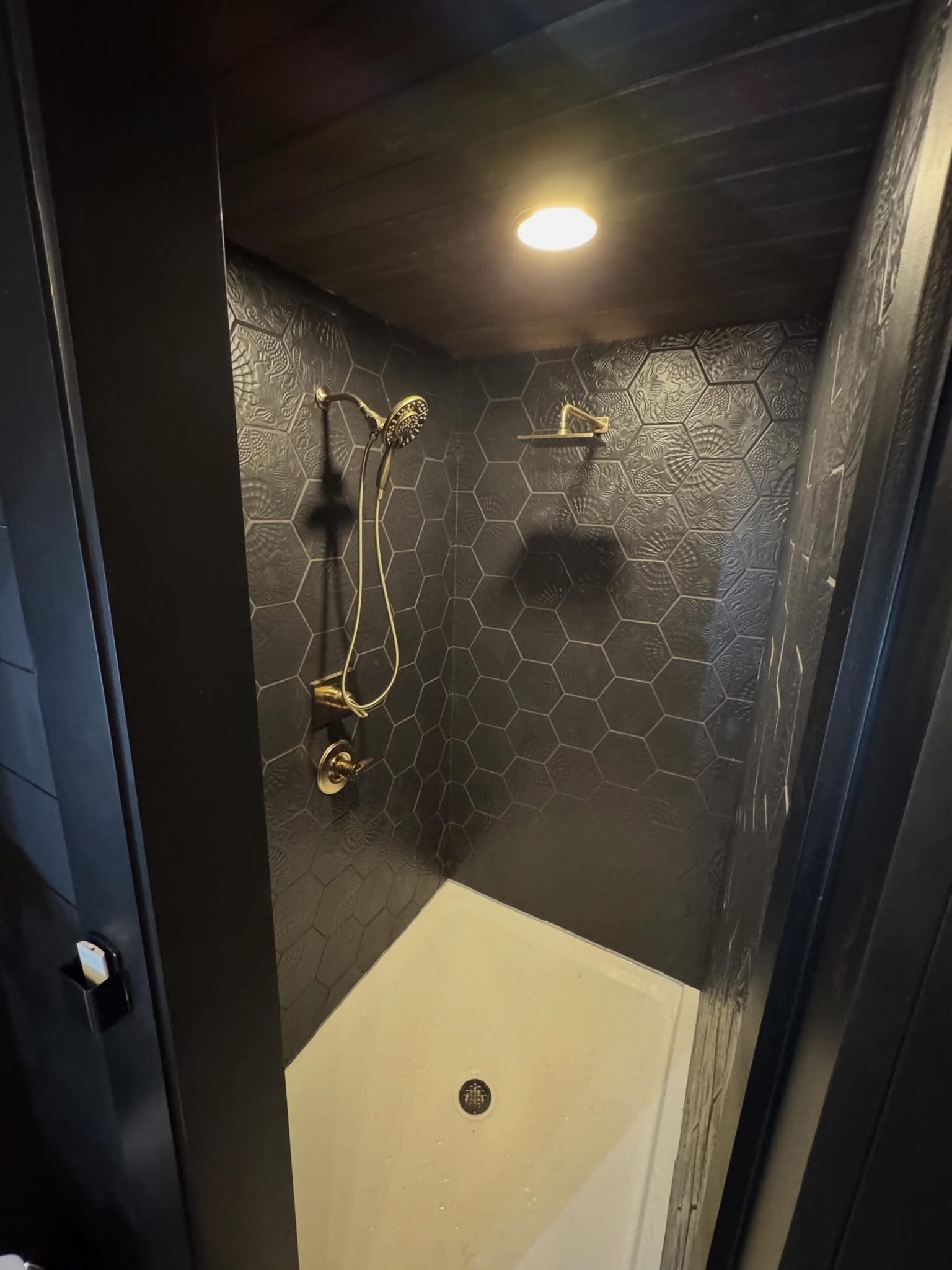 Updated walk-in shower with textured black tile and warm brass fixtures